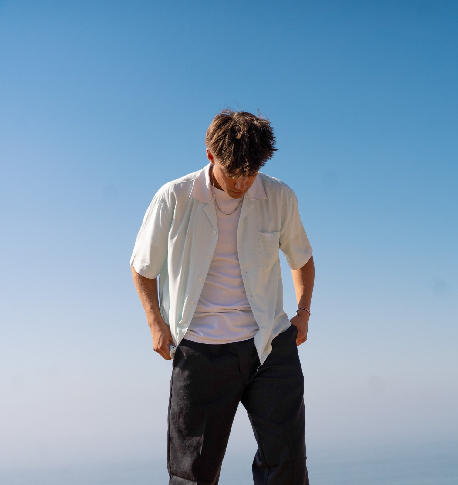 Male model wearing the Hypnotic Clothing HYP button-up shirt walking near the coast, relaxed minimal streetwear style.