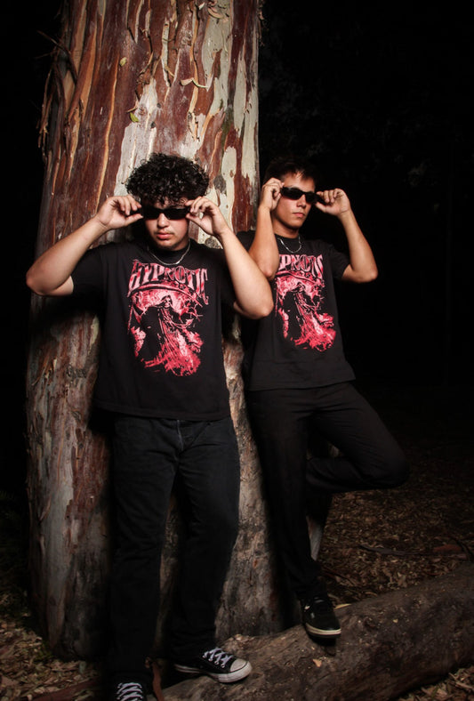Two Male models wearing the Hypnotic Clothing red Scythe graphic tee posing in a dark forest environment, moody streetwear portrait.