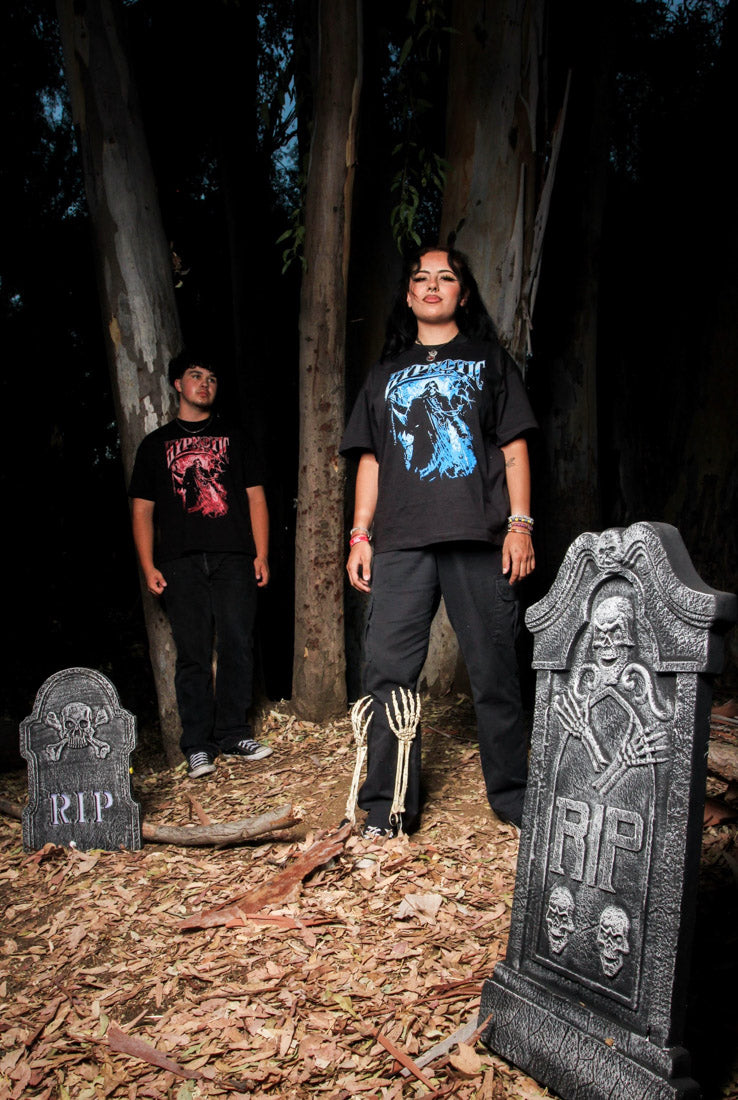 Models wearing Hypnotic Clothing Scythe graphic tees posing in a forest with tombstone props, gothic streetwear aesthetic.