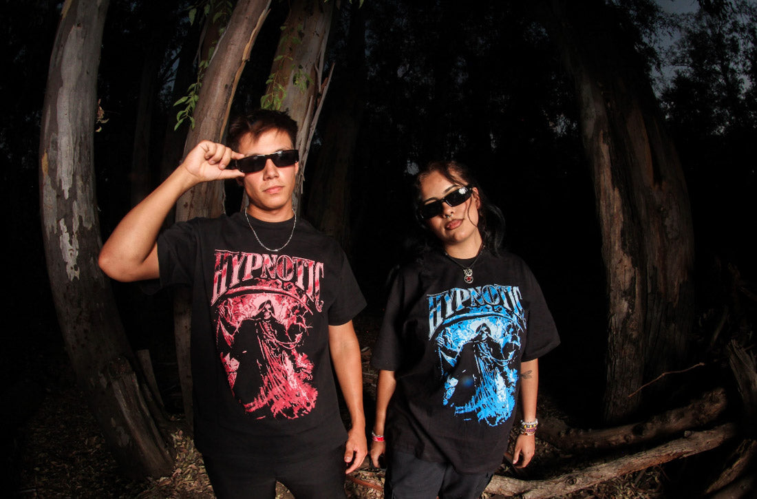 Two models wearing the Hypnotic Clothing Scythe graphic tees in red and blue standing in a nighttime forest setting, dark streetwear photography.