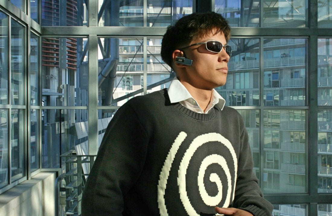 Male model wearing the Hypnotic Clothing Lost in the Matrix spiral sweater in a glass-walled library interior, futuristic streetwear photography.
