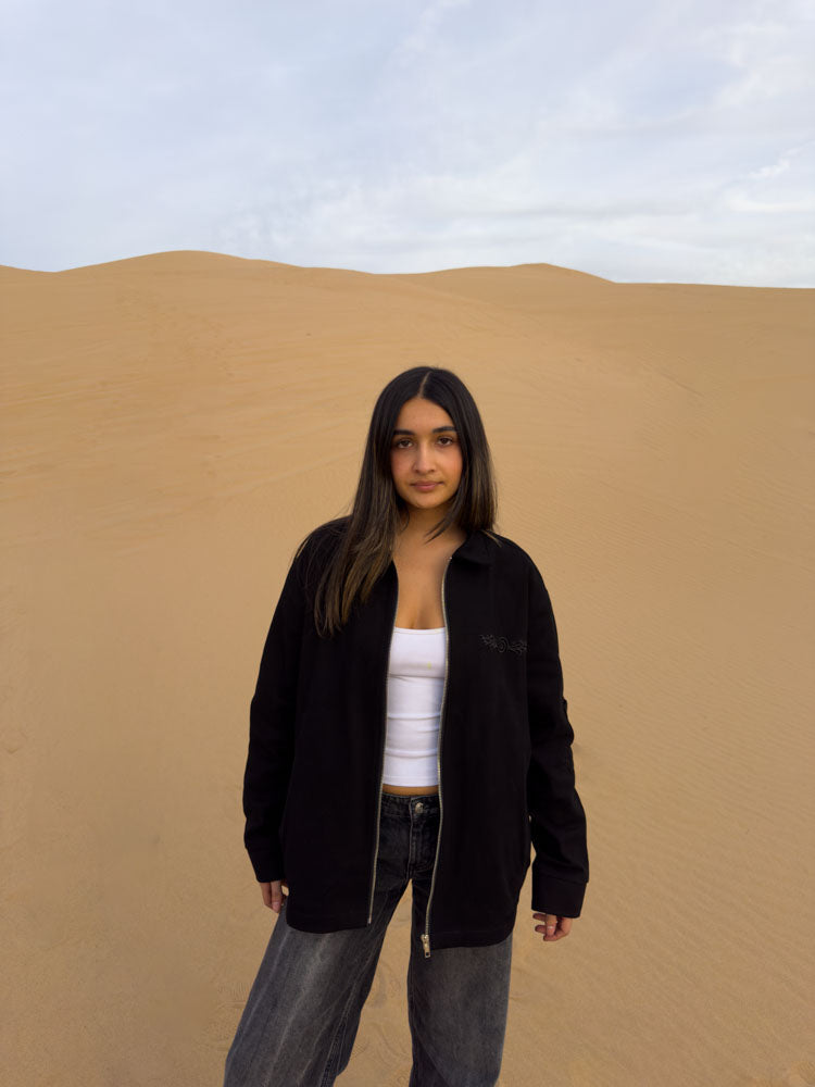 Female model wearing the Hypnotic Clothing Lucien black work jacket in desert landscape, modern streetwear photography.
