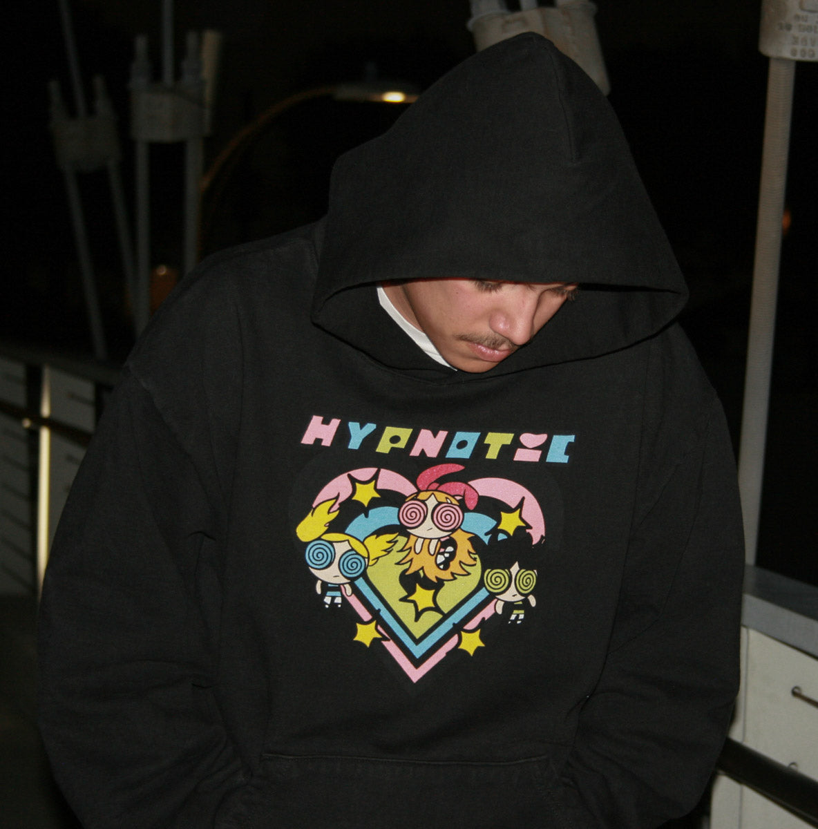 Close-up of model wearing the Hypnotic Clothing PPG graphic hoodie with hood up at night, bold graphic streetwear shot.
