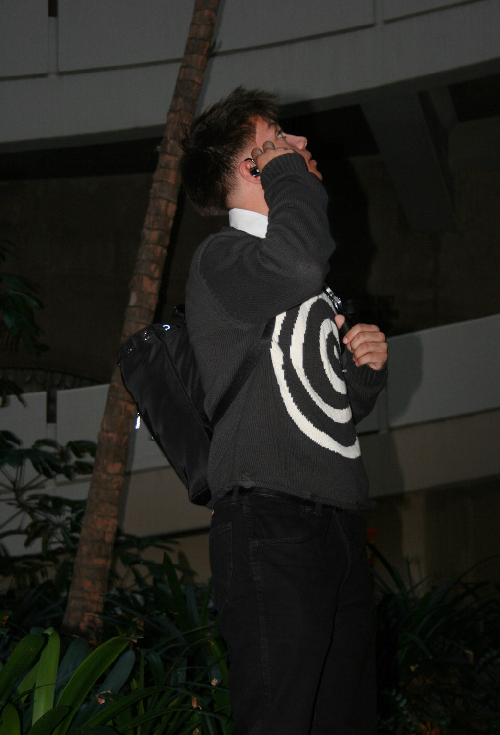 Side view of male model wearing the Hypnotic Clothing Lost in the Matrix spiral sweater inside a concrete spiral garage, modern streetwear editorial.
