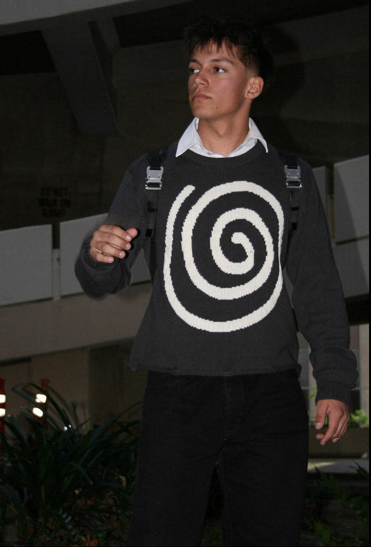 Male model wearing the Hypnotic Clothing Lost in the Matrix spiral sweater looking off-frame in concrete garage, clean streetwear portrait.