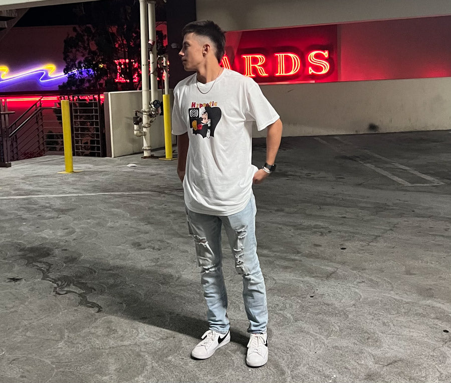 Person wearing Hypnotic Clothing ‘Mickey’ white streetwear T-shirt standing in a lit parking garage at night.