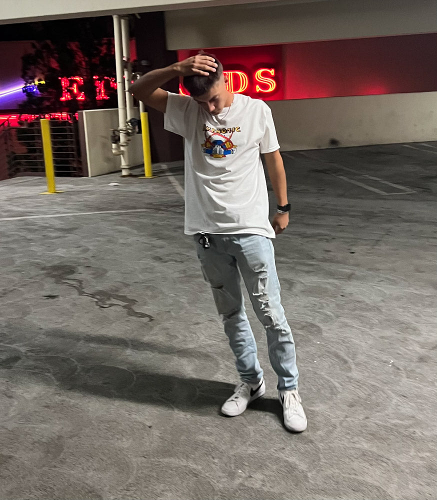 Model wearing Hypnotic Clothing ‘The Don’ white graphic tee in a parking garage, standing with hand on head.