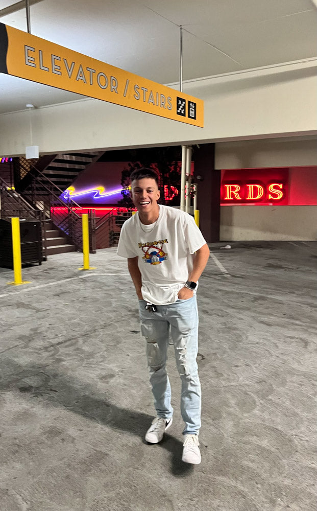 Model wearing Hypnotic Clothing ‘The Don’ white streetwear tee while standing and smiling in a lit parking garage.