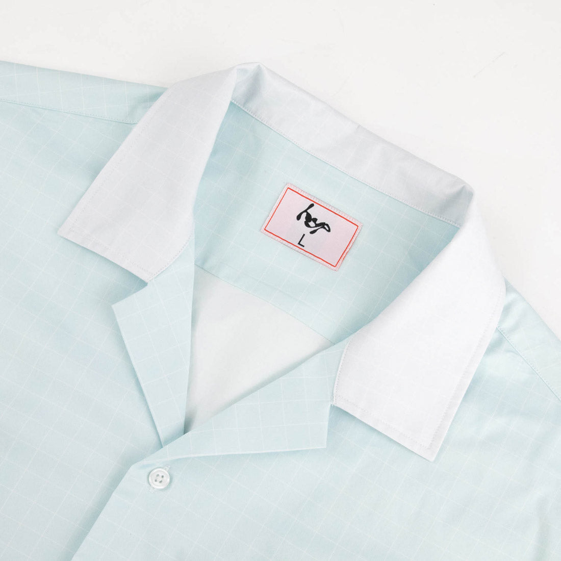 Close-up of Hypnotic Clothing HYP button-up shirt collar and branded neck tag, mint grid-pattern streetwear shirt.