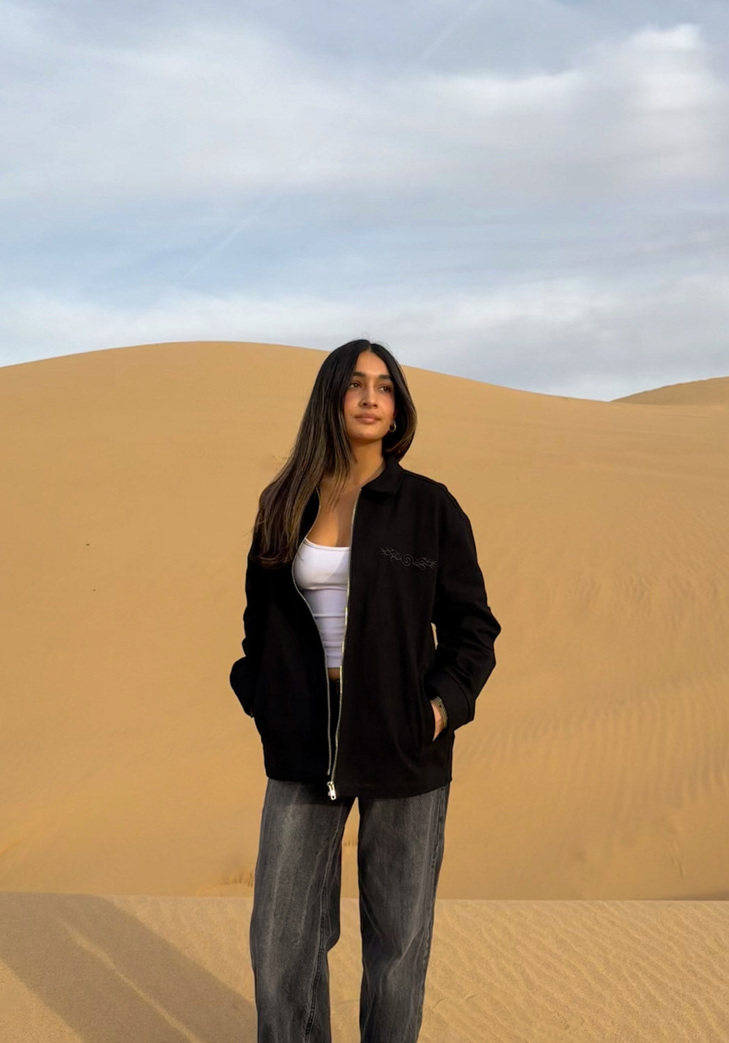 Female model wearing the Hypnotic Clothing Lucien black work jacket in the desert, looking straight ahead, dark modern minimalist streetwear photography.