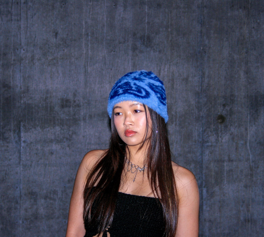 Close-up portrait of female model wearing the Hypnotic Clothing Magnate blue mohair knit beanie in front of textured concrete wall, moody streetwear photography.
