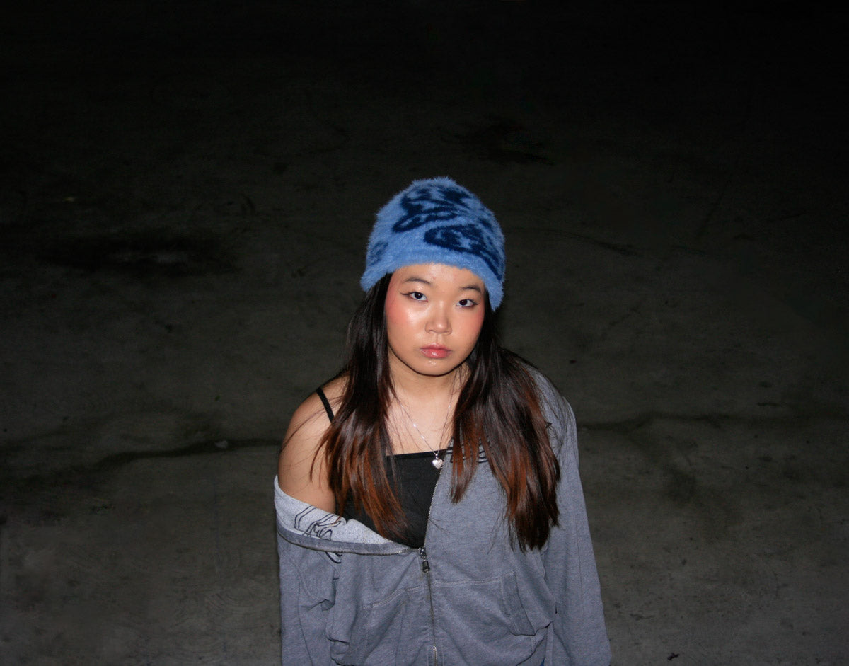 Female model wearing the Hypnotic Clothing Magnate blue mohair knit beanie against a dark outdoor background, contemporary streetwear look.