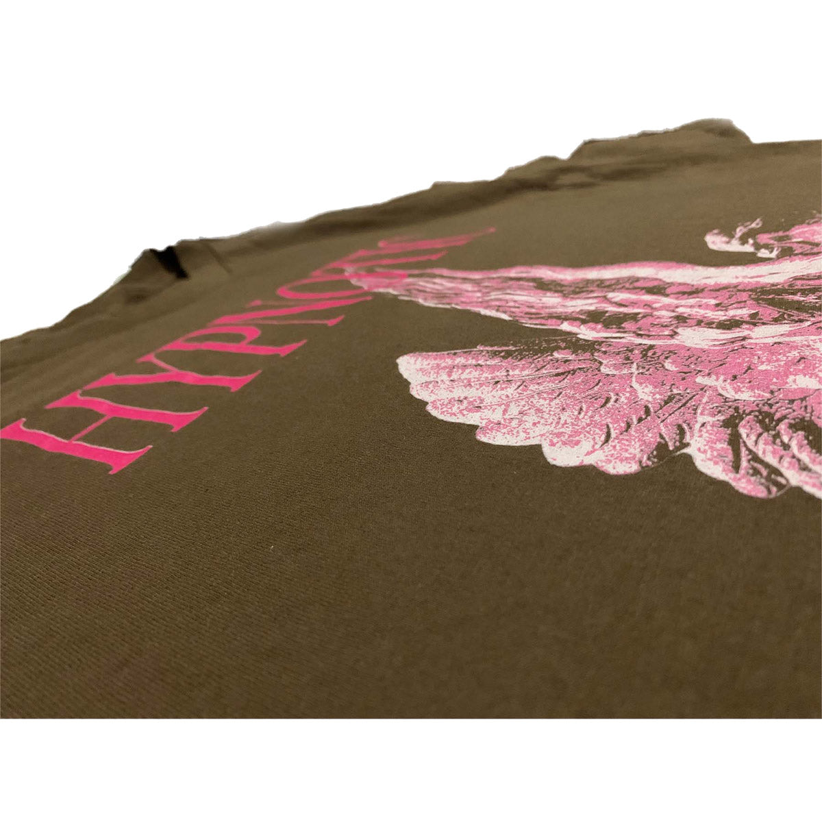 Close-up angled view of Hypnotic Clothing ‘Angel’ tee showing pink angel artwork and HYPNOTIC text on brown fabric.